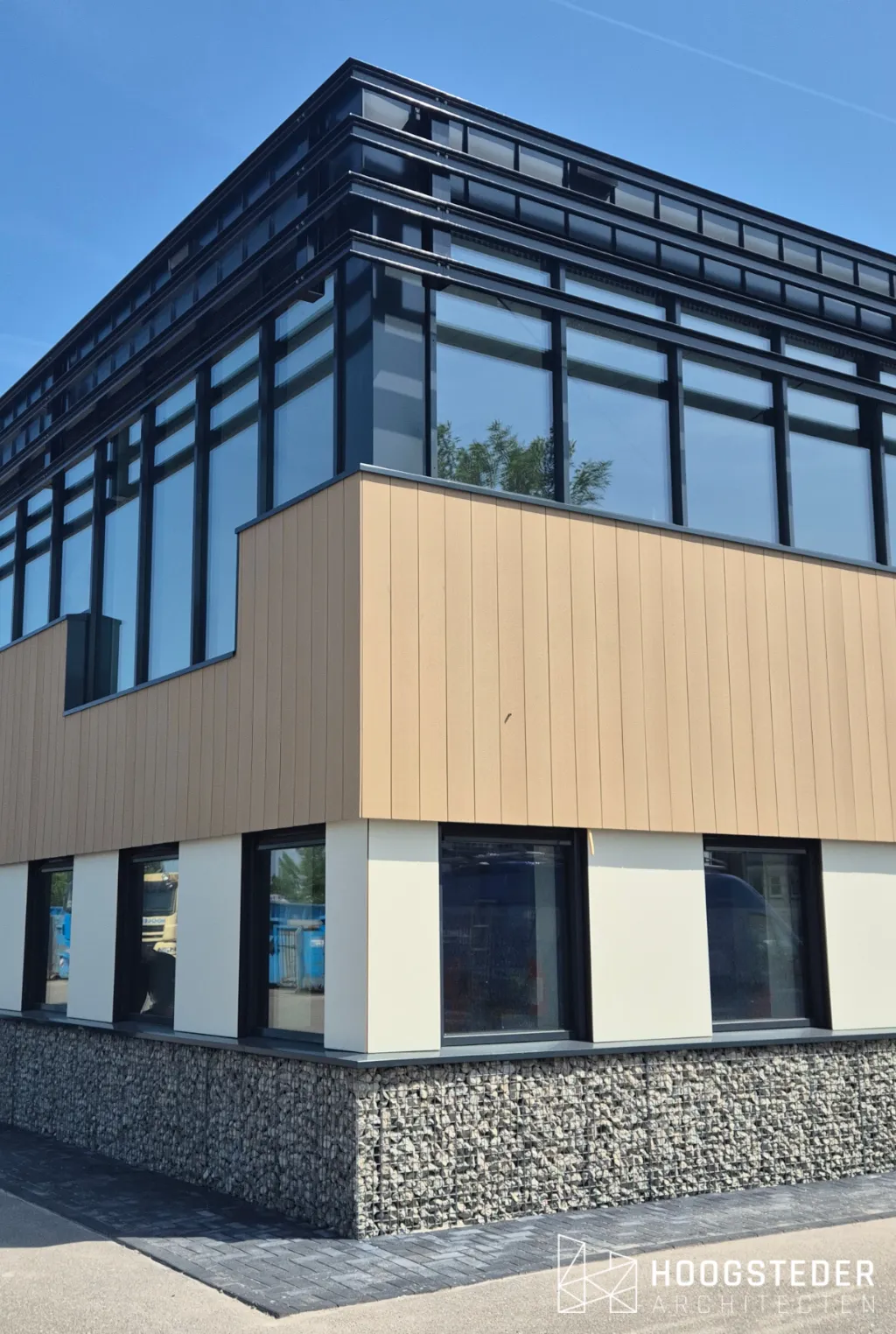 De gevel van dichtbij, met de overgang van glas naar houtkleurige geveldelen en de grintkorven langs de plint