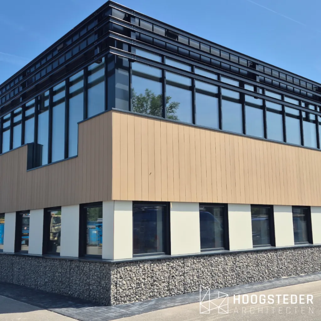 Hoek van het kantoorgebouw met donkere aluminium puien, een band van houtkleurige geveldelen en een plint van grintkorven