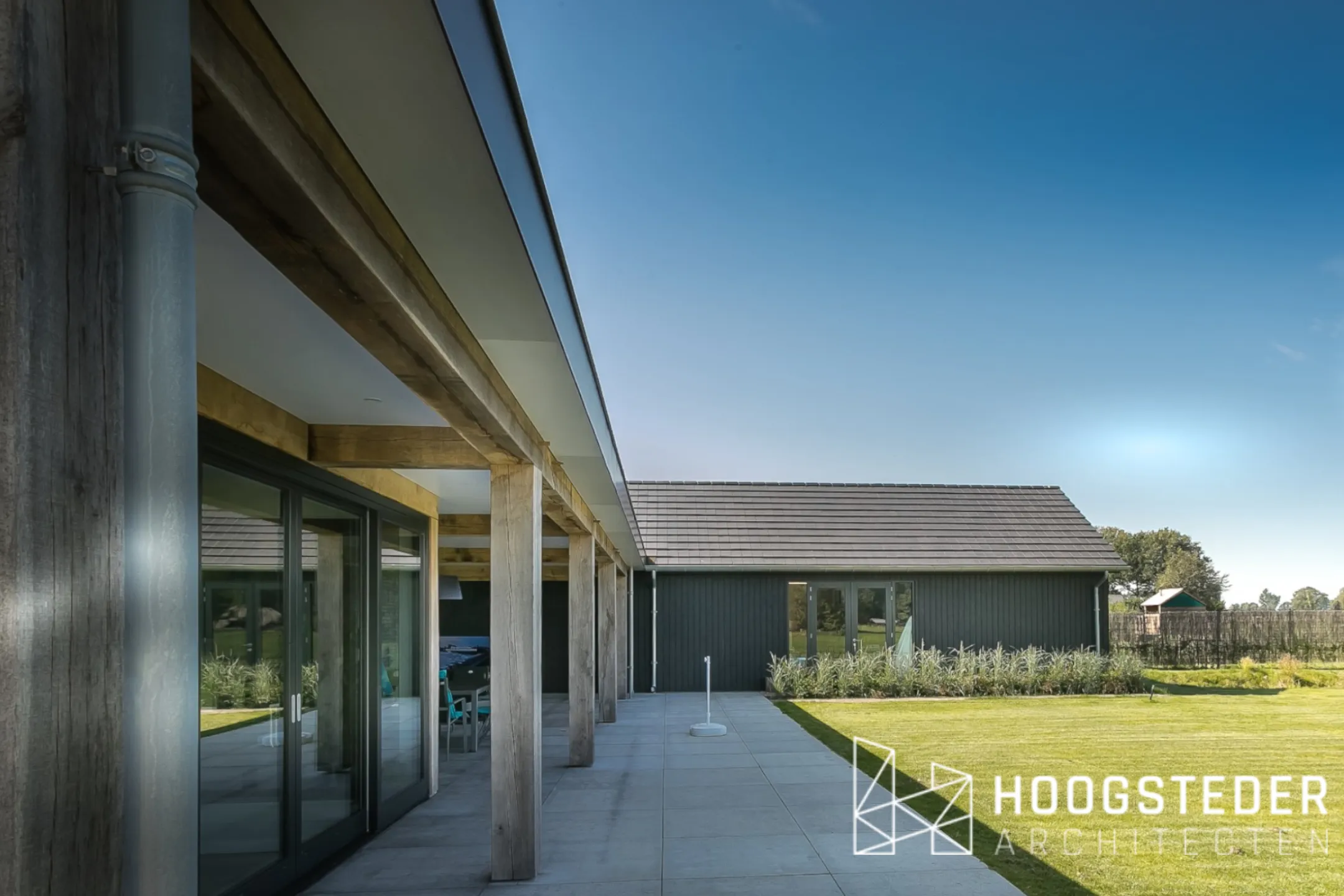 De eikenhouten balken en kolommen van de uitbouw in een regelmatig ritme, met het terras en de tuin ernaast