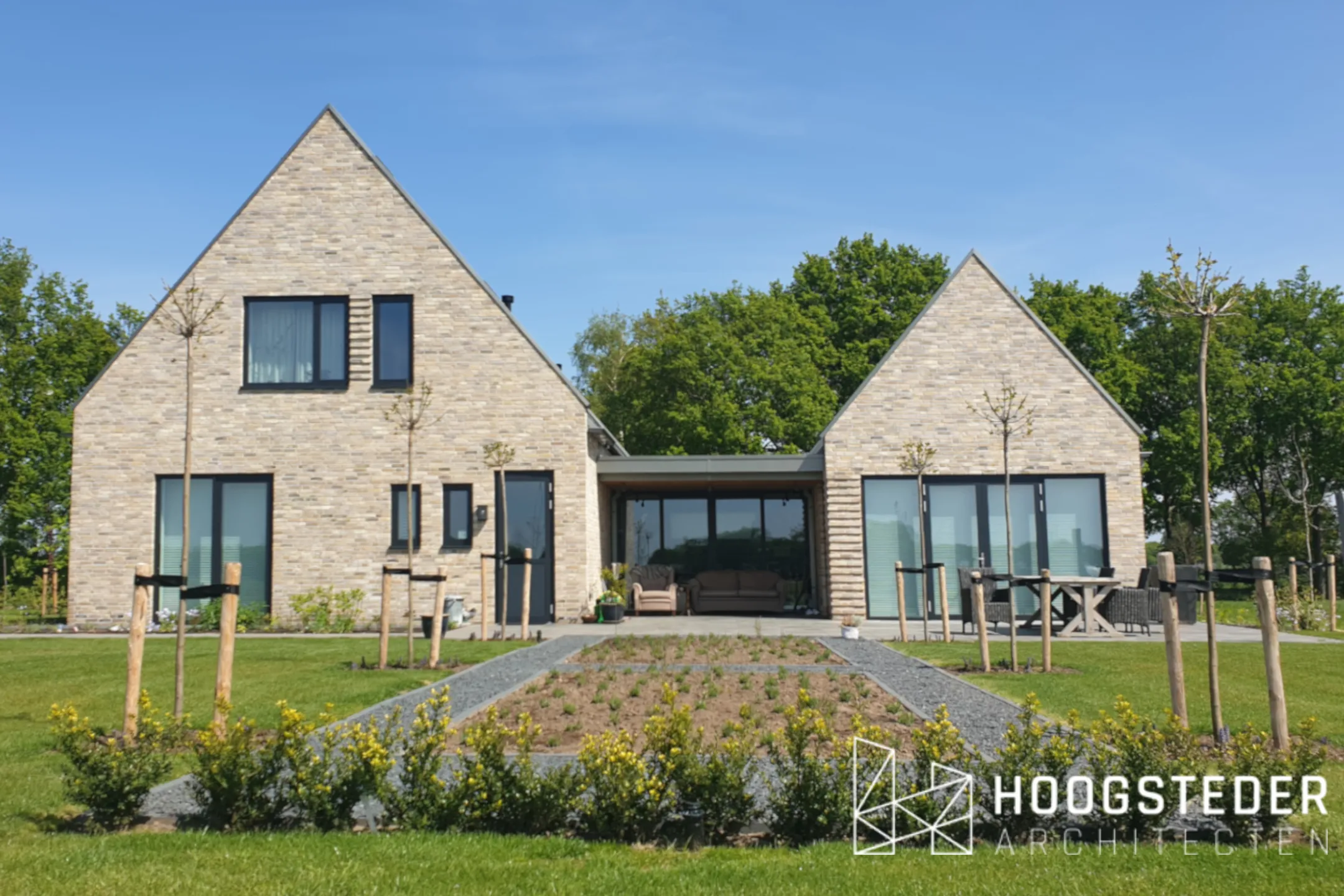 Moderne woning van twee kapvolumes in lichte baksteen met een laag tussenlid van hout en glas