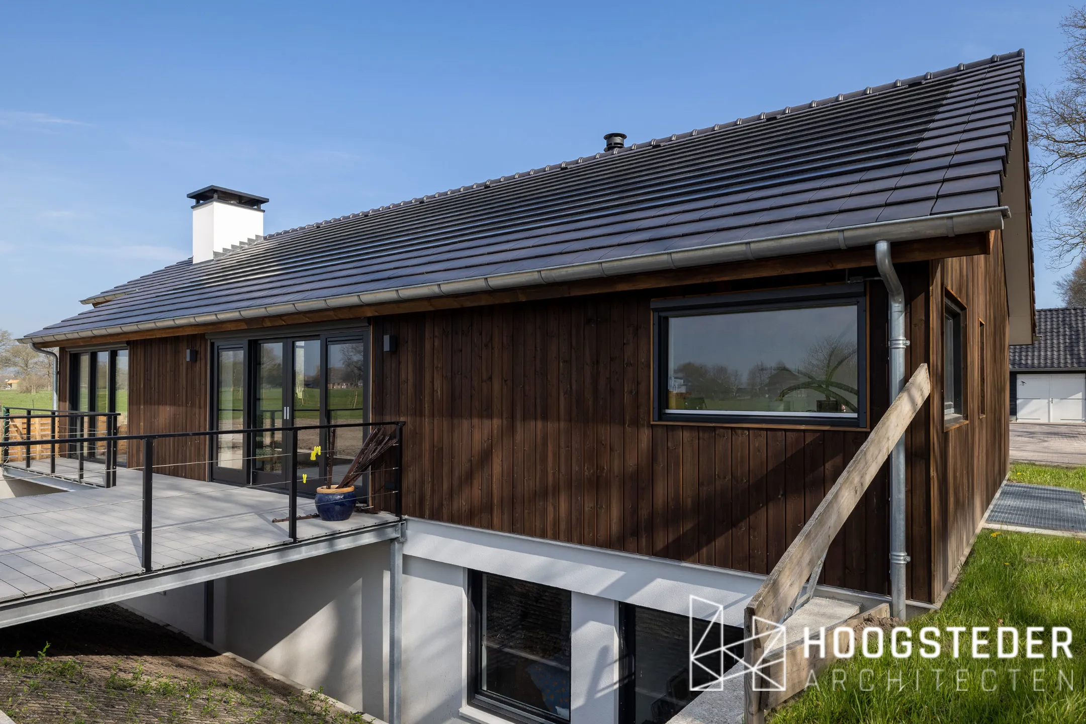 Moderne schuurwoning op de Veluwe met donkere houten gevel, vlakke dakpannen en de ramen van het souterrain onder het terras