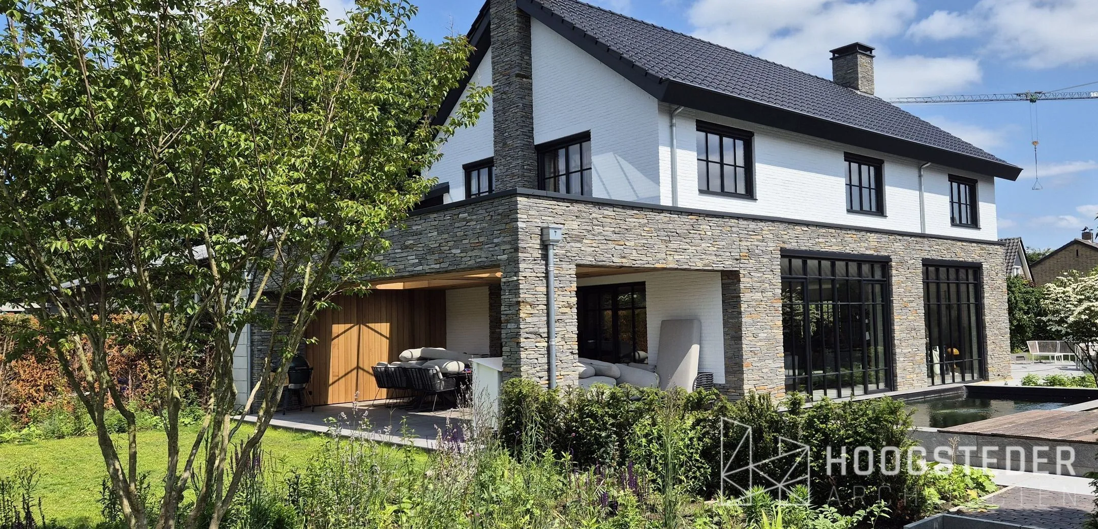 Villa met natuurstenen plint en wit metselwerk erboven, met een overdekte veranda en een vijver in de tuin