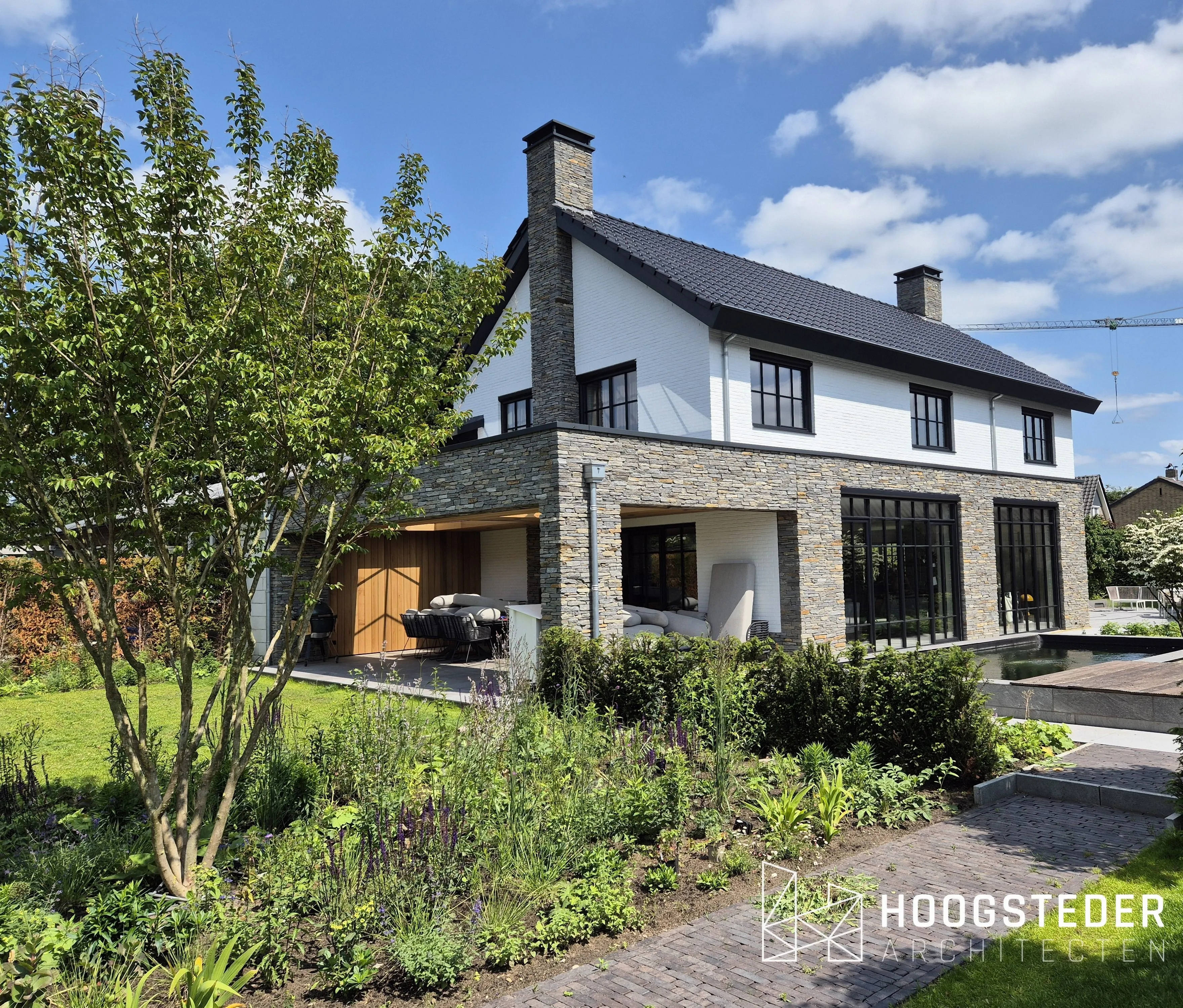 Villa met natuurstenen plint en wit metselwerk erboven, met een overdekte veranda en een vijver in de tuin