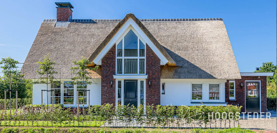 Rietgedekte villa met rode baksteen en een hoge glazen topgevel boven de entree