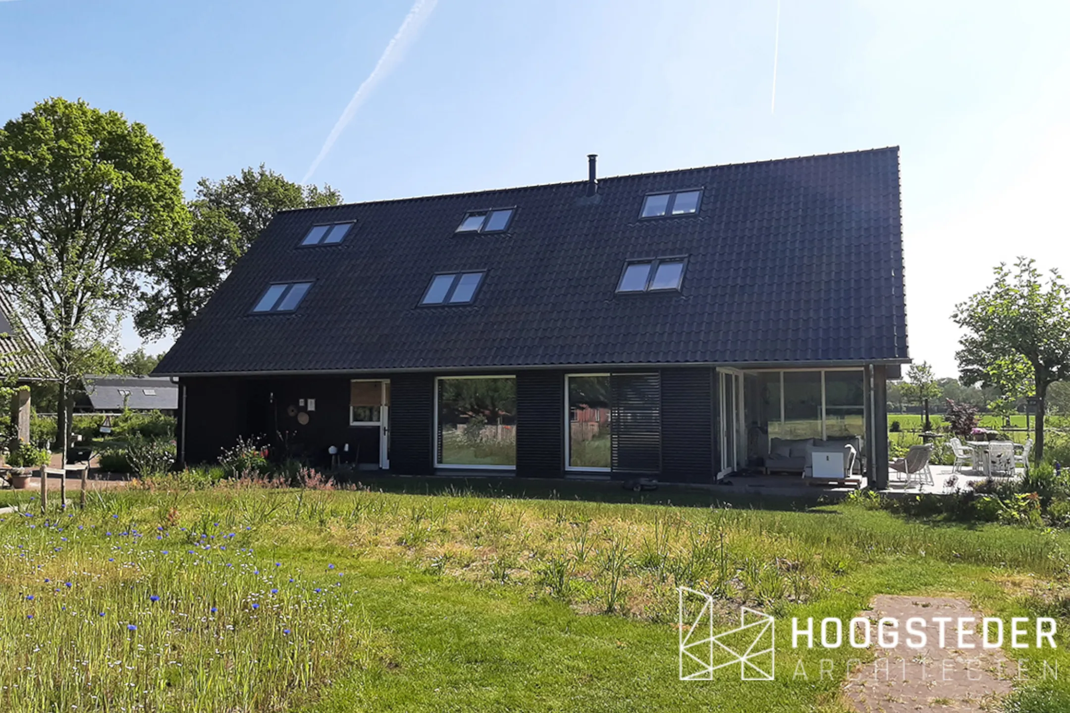 De schuurwoning vanaf de tuin, met een groot dakvlak in gemêleerde donkere dakpannen en dakramen