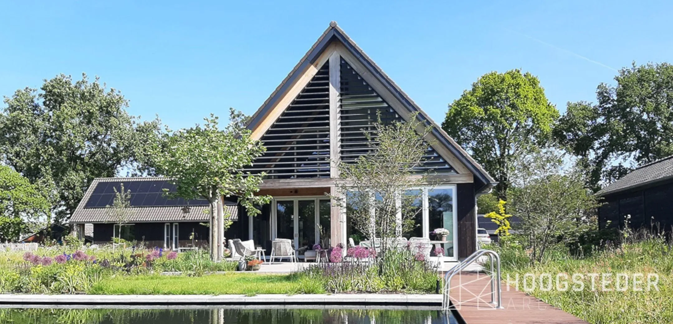 De natuurlijke zwemvijver in de achtertuin, met een vlonder langs de rand en de woning erachter