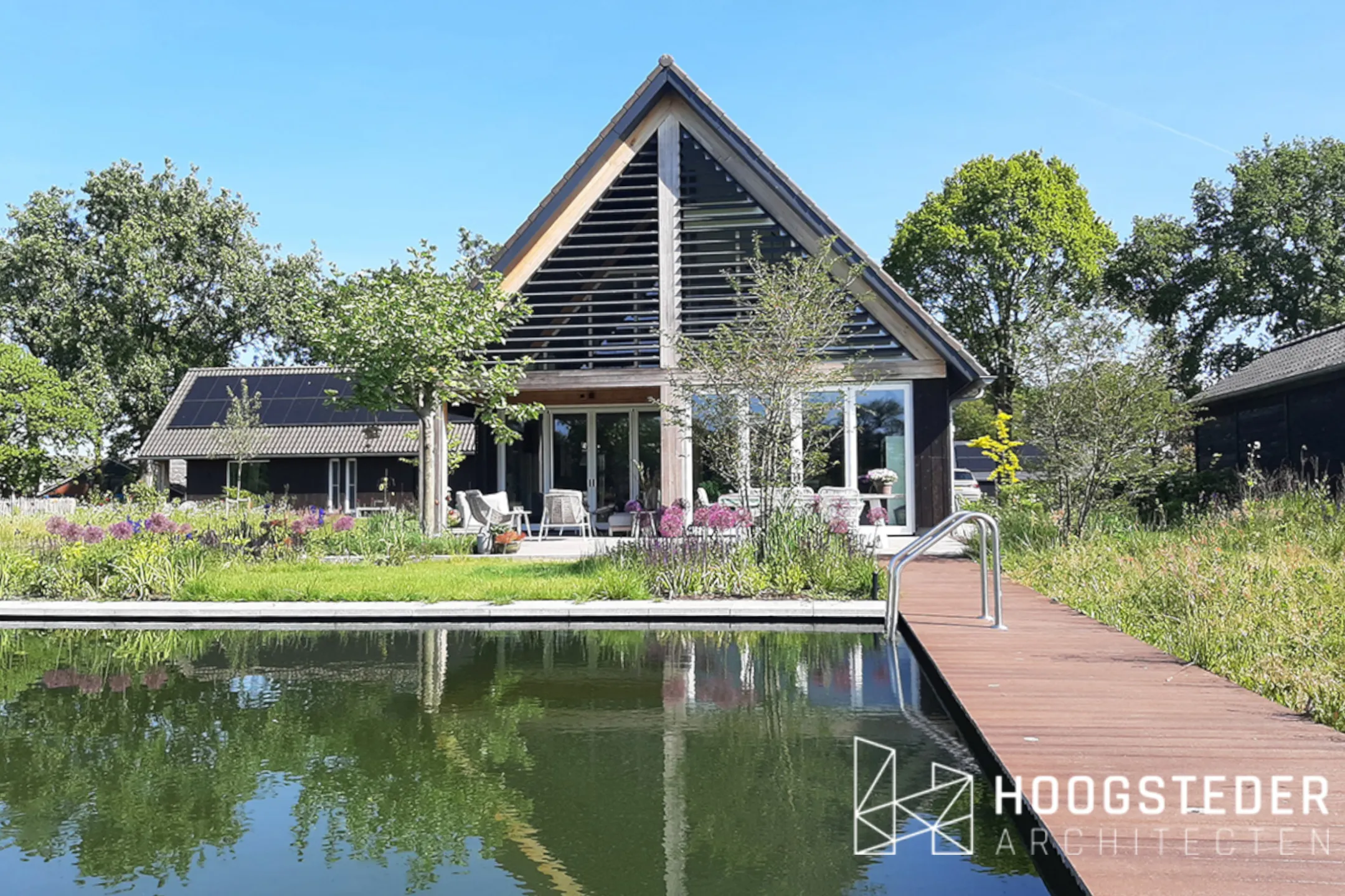 De natuurlijke zwemvijver in de achtertuin, met een vlonder langs de rand en de woning erachter
