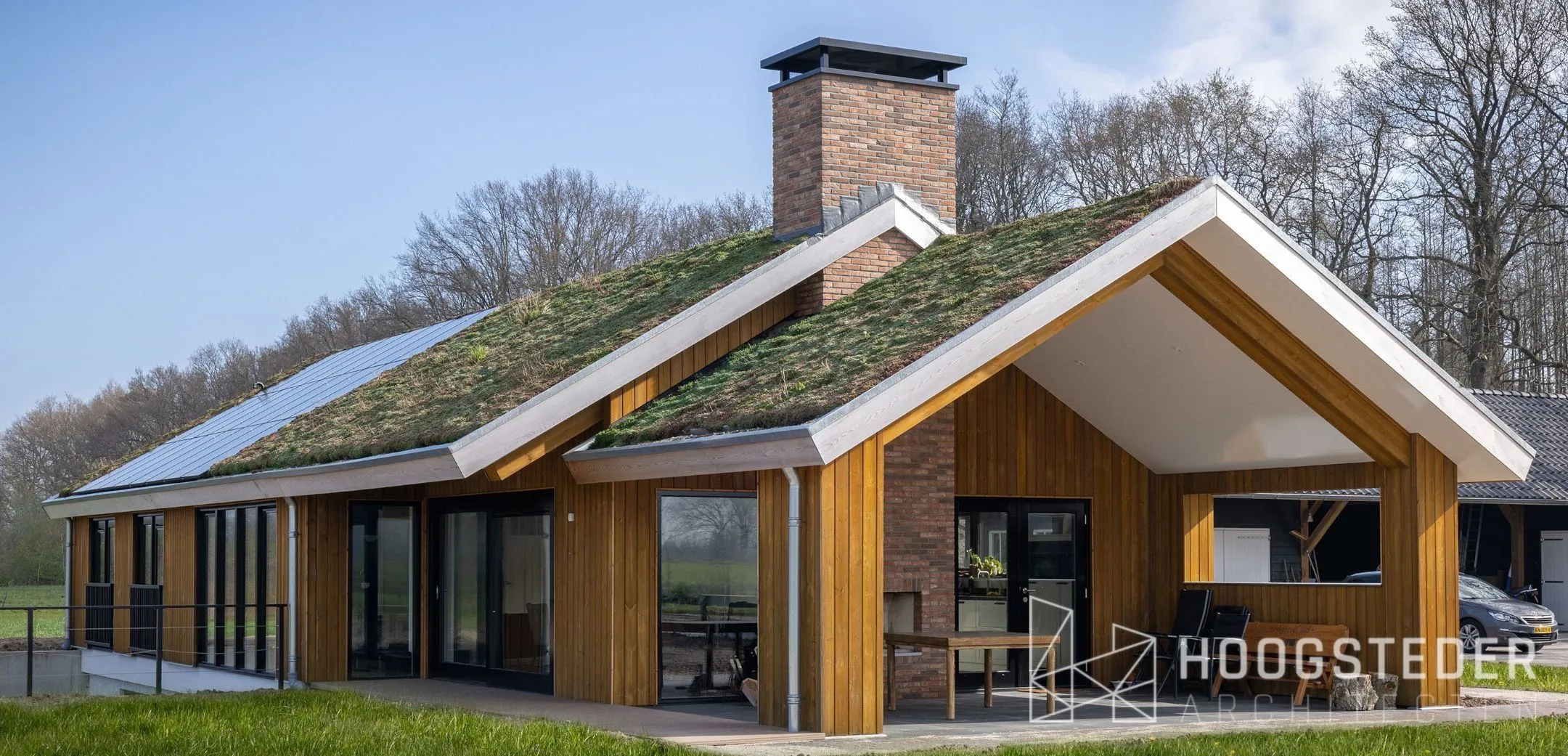Een van de twee schuurwoningen in Emst, met naturel houten gevels, een groen dak van mos en sedum en een overdekte veranda onder de kap