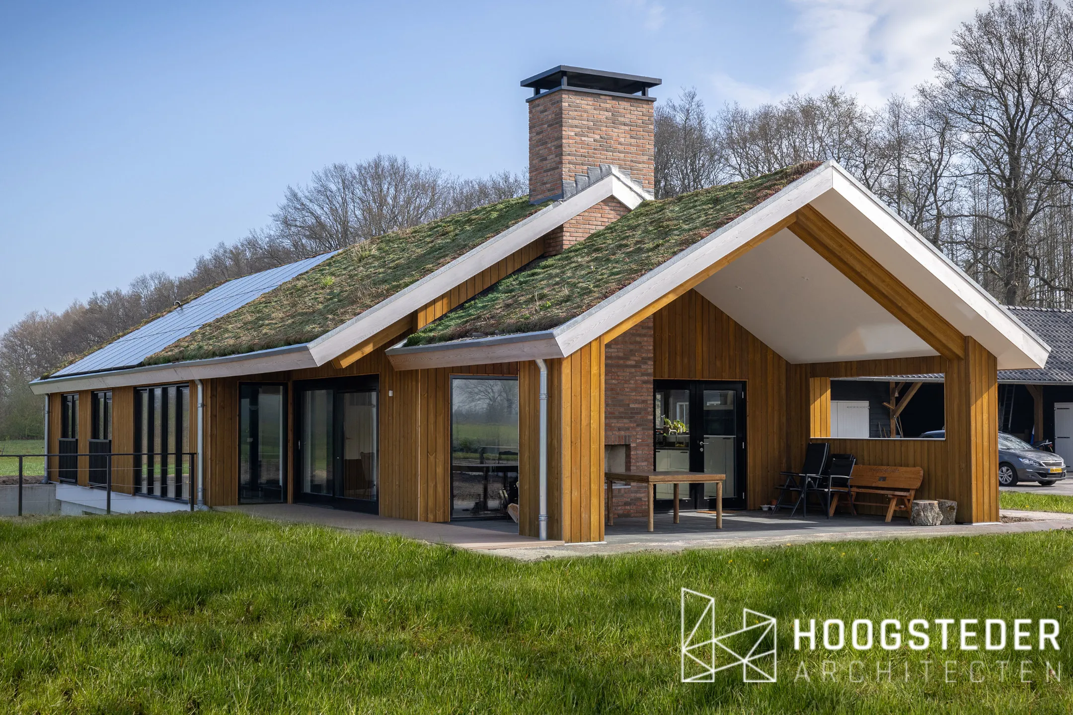 Een van de twee schuurwoningen in Emst, met naturel houten gevels, een groen dak van mos en sedum en een overdekte veranda onder de kap