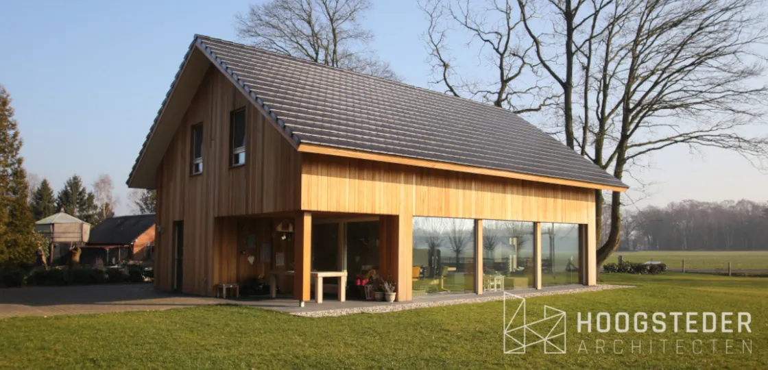 Schuurwoning met verticale houten gevel en een diepe overkapping over de glazen pui