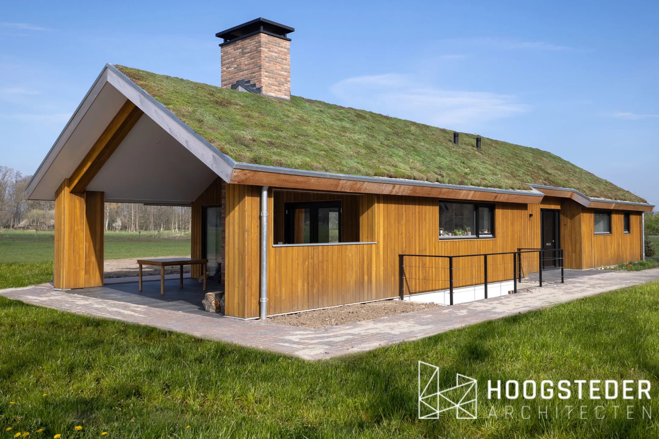 Houten schuurwoning op de Veluwe met een veranda onder de doorgetrokken kap en weiland eromheen