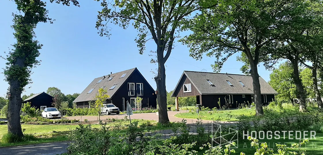 Twee zwarte schuurwoningen op een erf met oude eiken langs de oprit