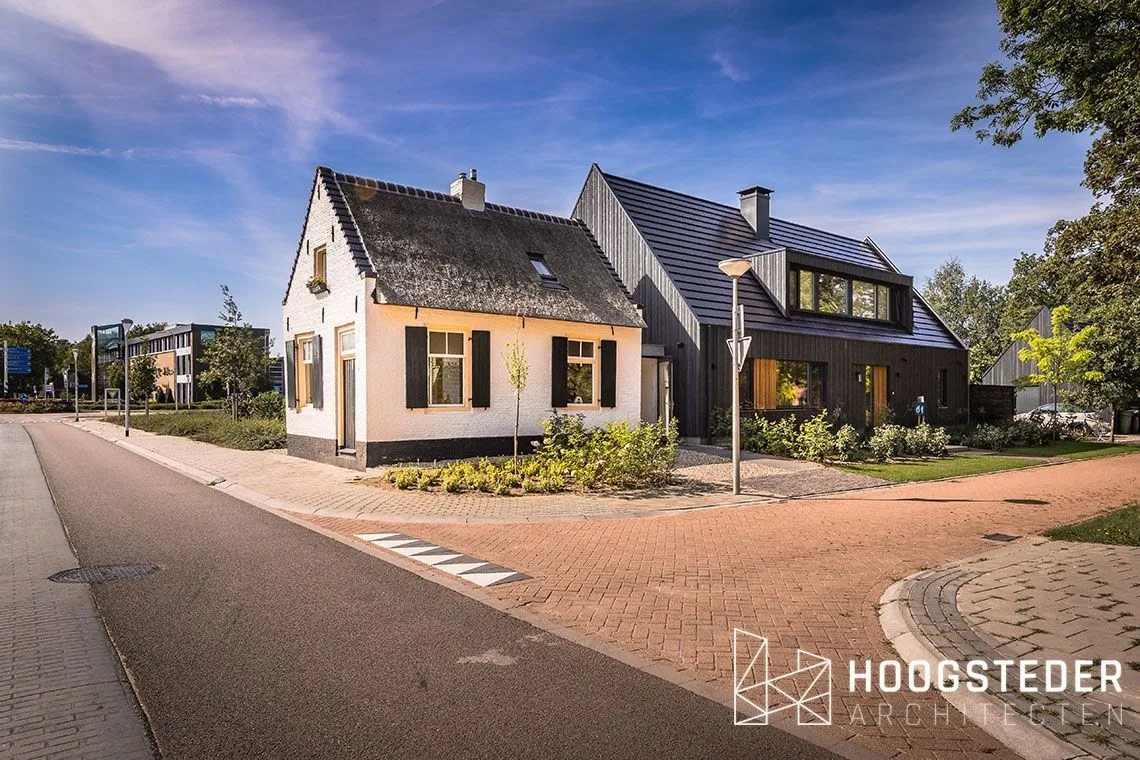 Wit gepleisterd tolhuisje met daarachter een zwarte nieuwbouwwoning met houten gevel