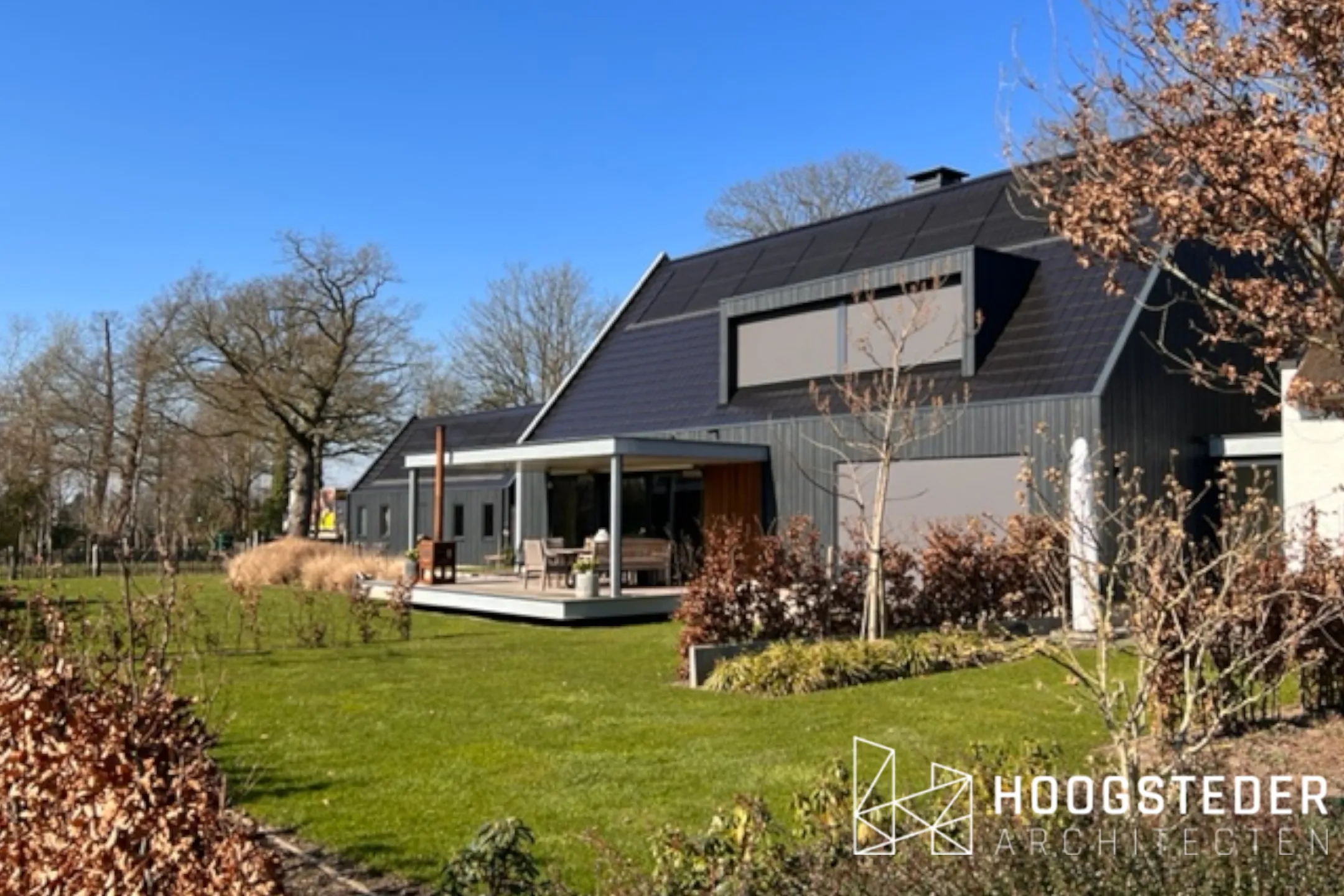 De tuinzijde van de nieuwbouw met grote glasvlakken, een stalen veranda en zonnepanelen in het dakvlak