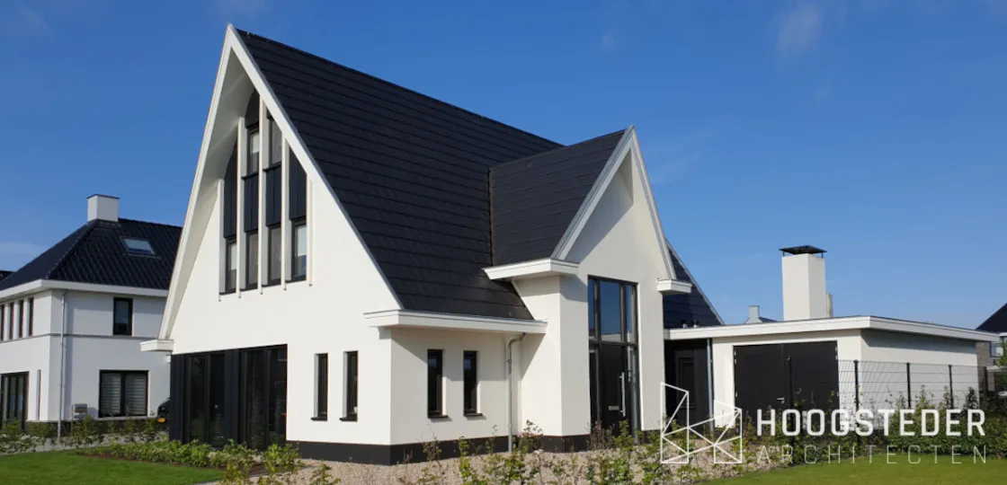 Witte woning met steile zwarte kap, smalle raamstroken en een zwart houten aanbouw