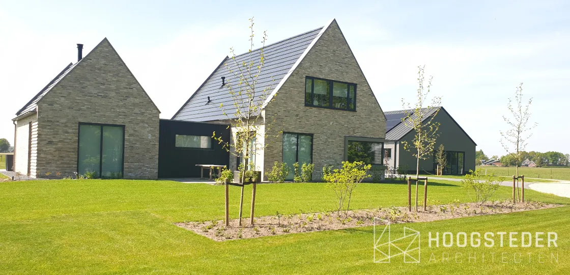 Woning van lichte baksteen met twee kappen en een donker verbindingsvolume in het weiland